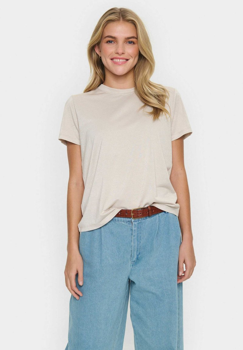 Beige t-shirt med kort ärm och avslappnad passform, tillverkad av mjukt tyg. Kombinerad med högmidjade ljusblå jeans och ett brunt bälte.
