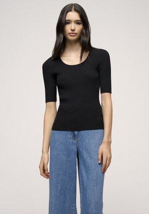 Top corto a maniche corte ribbed nero con scollo a barca, silhouette aderente e texture morbida, abbinato a jeans a gamba larga azzurri.