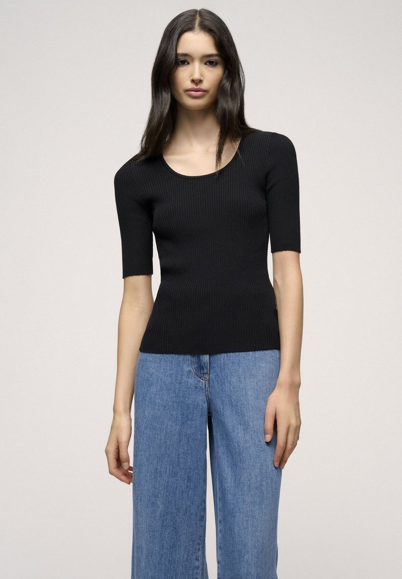 Schwarzes geripptes T-Shirt mit kurzen Ärmeln und Rundhalsausschnitt, figurbetontem Schnitt und weicher Textur, kombiniert mit hellblauen weit geschnittenen Jeans.