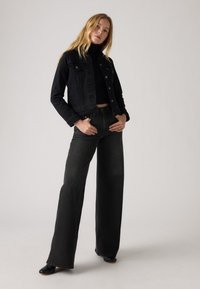Melnas denim jaka ar saīsinātu dizainu un pogu aizvēršanām, saderota ar augsto vidukli melnām platām biksēm un elegantu melnu apavu pāri.