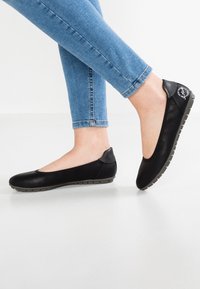 Black flat shoes with a smooth leather finish and rubber sole. Rounded toe design and contrasting gray heel accent.