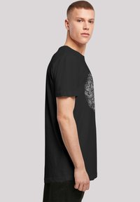 Svart bomull T-skjorte med en detaljert hvit grafisk design på forsiden. Korte ermer og klassisk rund hals.