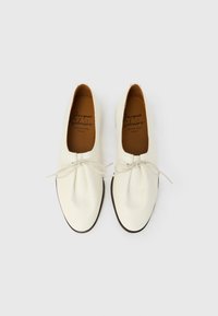 Chaussures en cuir blanc à finition texturée, avec un bout arrondi, des lacets fins et une semelle contrastante foncée. Intérieur doublé en marron.