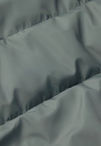 Tkanina kurtki puchowej w stonowanym odcieniu szarości, charakteryzująca się gładką, błyszczącą fakturą oraz poziomymi, przeszytymi panelami, które tworzą pikowany wygląd.