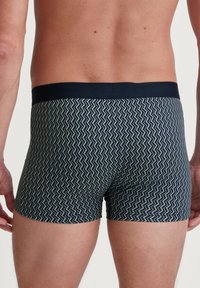 Navy blue boxer shorts with a zigzag pattern in green. Features a stretchy waistband, medium length, and a smooth fabric texture.