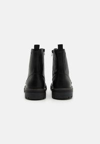 Botas de cuero negras hasta el tobillo con una textura suave, que cuentan con cierres de cremallera en la parte trasera, suelas de goma resistentes y un diseño minimalista.