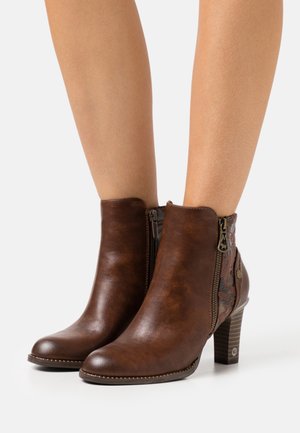 Brown ankle boots with a smooth leather texture, side zippers, patterned accents, and a wooden heel. Rounded toe design.