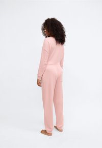 Σετ άνετης ένδυσης σε ανοιχτό ροζ χρώμα με μακριά μανίκια, άνετη εφαρμογή, ραβδωτή υφή και τσέπες στο πίσω μέρος του παντελονιού.