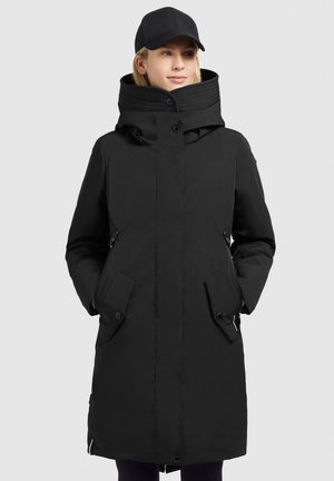 Parka nera isolata con colletto alto, tasche laterali e chiusura nascosta. Texture liscia e design elegante. Accompagnata da un berretto nero.