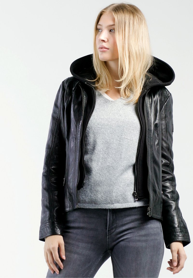 Schwarze Lederjacke mit großer Kapuze, Reißverschlussfront, gerippten Bündchen, getragen über einem grauen Pullover, kombiniert mit grauen Jeans.