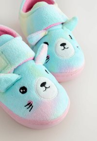 Des chaussons flous bleus et roses ornés d'un joli visage d'ours, avec une texture douce, une forme ronde et des oreilles. Accentué de détails noirs pour les yeux et le nez.
