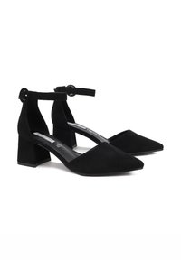 Scarpe alla caviglia in suede nero con tacco blocco, punta appuntita e accentuazione a fibbia circolare. Texture liscia e design minimalista.