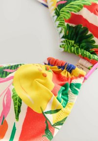 Värvikas bikiinitop troopiliste lillemustritega, peamiselt kollane punaste, roheliste ja roosade aktsentidega, valmistatud venivast kangast.