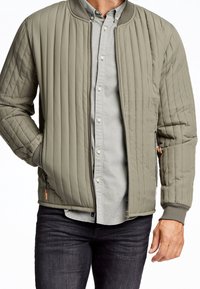 Giubbotto bomber imbottito di colore verde oliva con design a righe orizzontali, colletto e polsini a costine; dotato di tasche laterali con zip.