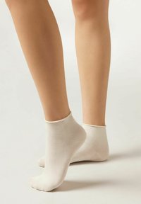 Calcetines tobilleros beige hechos de un material suave con una textura lisa y un acabado de puño acanalado, que presentan un diseño simple y sin costuras.