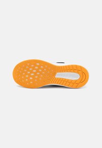 Semelle de chaussure en caoutchouc orange texturé avec des rainures circulaires et ovales, mettant en avant les motifs d'adhérence et de traction.