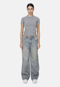 Szara, krótko krojona koszulka z krótkim rękawem, w połączeniu z jasnoniebieskimi spodniami typu wide-leg. Białe trampki dopełniają zestaw.