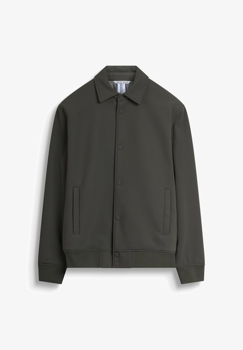 Veste légère vert foncé avec un col, des boutons-pression, des poches latérales et des poignets côtelés à l'ourlet, fabriquée dans un matériau lisse et texturé.