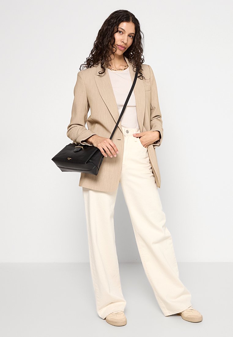 Beige op maat gemaakte blazer over een lichte top, gecombineerd met crèmekleurige wijde broek. Zwarte handtas met gouden hardware. Casual sneakers maken de look af.