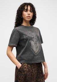 Σκούρο γκρι κοντομάνικο crop top με διακοσμητικό γραφικό καρδιάς με κρόσσια και κείμενο. Συνδυάζεται με φούστα με λεοπάρ μοτίβο.