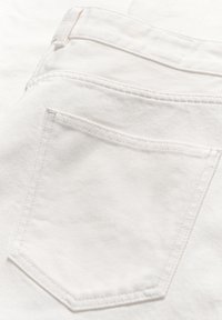 Jeans de mezclilla blanca que presentan un bolsillo trasero con costuras visibles. La tela es suave con una ligera textura, lo que resalta la durabilidad y el estilo.