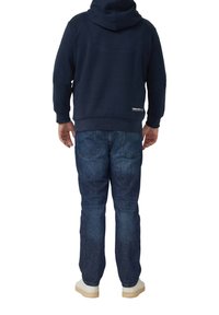 Granatowa bluza z kapturem o fakturowanym wykończeniu, zestawiona z niebieskimi dżinsami z wyblakłymi akcentami i tylnymi kieszeniami. Całość dopełniają jasne tenisówki.