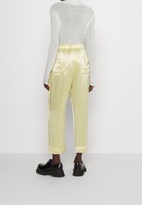 Ljusgula satinbyxor med elastisk midja, cropped längd och två bakfickor, kombinerade med svarta skor med kraftig sula.