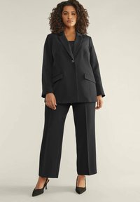 Blazer nero con un singolo bottone, rever a punta e due tasche frontali abbinato a pantaloni a gamba larga. Tessuto morbido, design professionale.