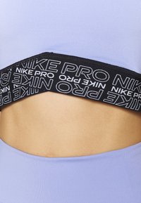 Närbild av midjan som bär ljuslila träningstights och ett svart Nike Pro midjeband med vit brandingtext.
