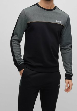 Man wearing a black and gray long-sleeve sweatshirt and matching black pants with "BOSS" logo on chest and thigh.
