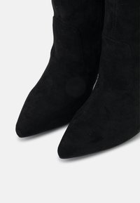 Bottines en daim noir à bout pointu et silhouette élégante, présentant une texture lisse et des détails de couture minimalistes.