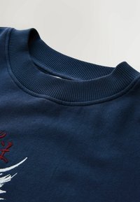 Granatowy bawełniany sweter z prążkowanym, okrągłym dekoltem i wyszywanymi czerwonymi oraz białymi akcentami, prezentujący gładką, fakturowaną tkaninę.