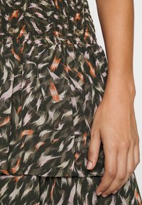 Robe à volants à motifs floraux en vert foncé, avec un corsage smocké et une jupe plissée ornée de nuances d'orange et de rose en coup de pinceau.
