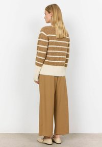 Bruine en crèmekleurige gestreepte gebreide trui met geribbelde zoom, beige wijde broek en lichte schoenen. Zachte textuur, relaxte pasvorm en casual stijl.