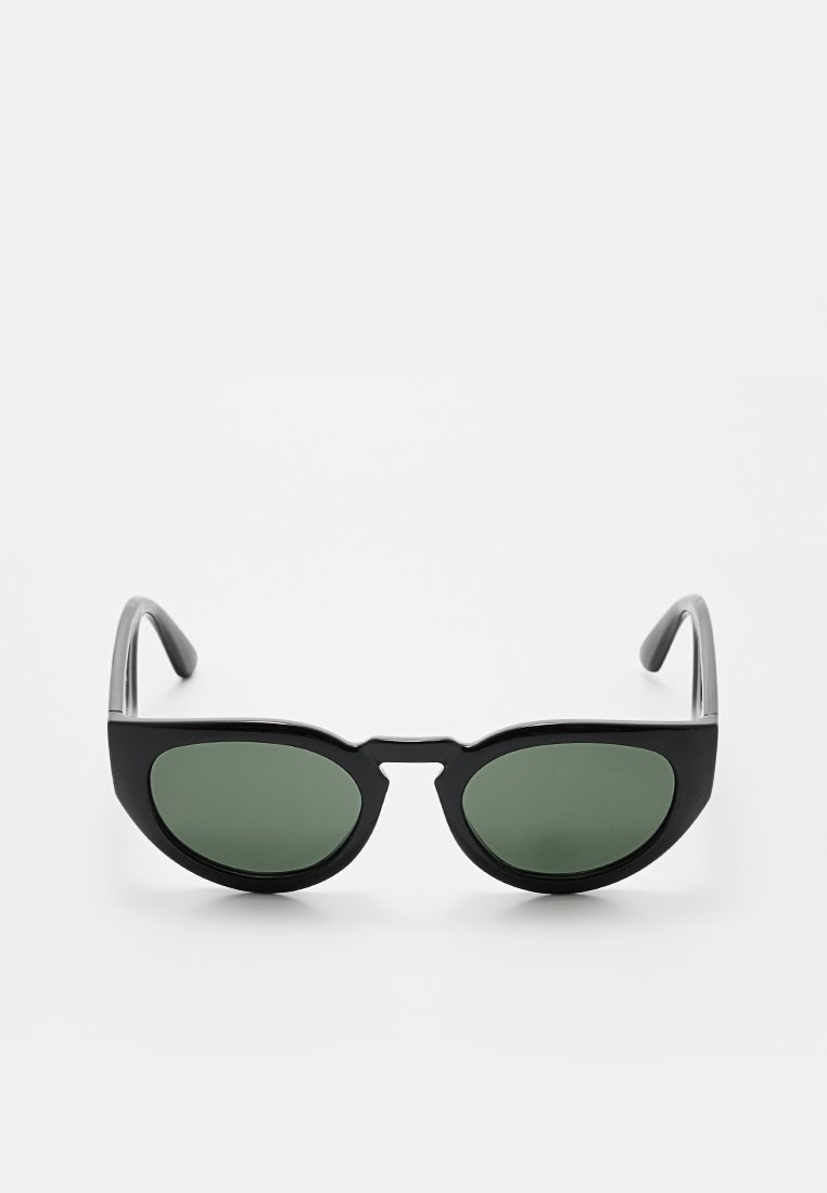 Lunettes de soleil noires en forme d'œil de chat avec verres verts, monture en plastique et branches argentées élégantes. Présente un design de pont distinctif.
