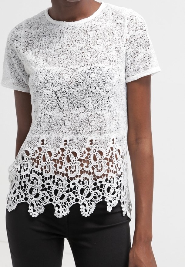 Top bianco in pizzo con maniche corte, caratterizzato da un delicato motivo in crochet floreale all'orlo, sovrapposto a una parte inferiore nera uniforme.