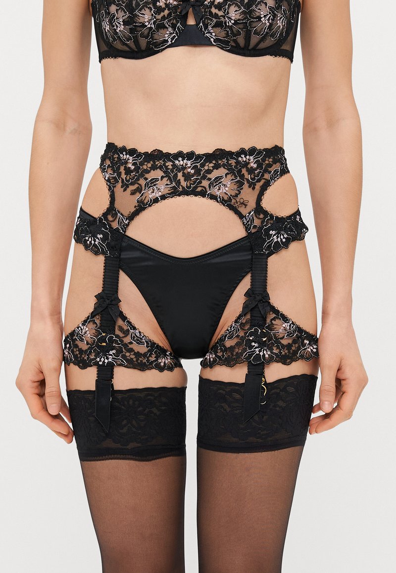 Črni kompleti perila, ki vključuje cvetlični čipkast material, satenske poudarke in prosojne panele. Vključuje pas za nogavice z nastavljivimi trakovi in nogavice do stegen.