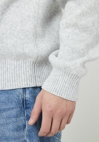 Pull gris côtelé avec un tricot texturé, doté d'un détail de poignet replié, associé à un jean en denim bleu. Accent sur le tissu et la coupe.