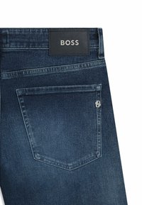 Mörkblå denimjeans med en läderlapp märkt "BOSS" på bakre midjebandet och en distinkt ficka med silverdetalj.