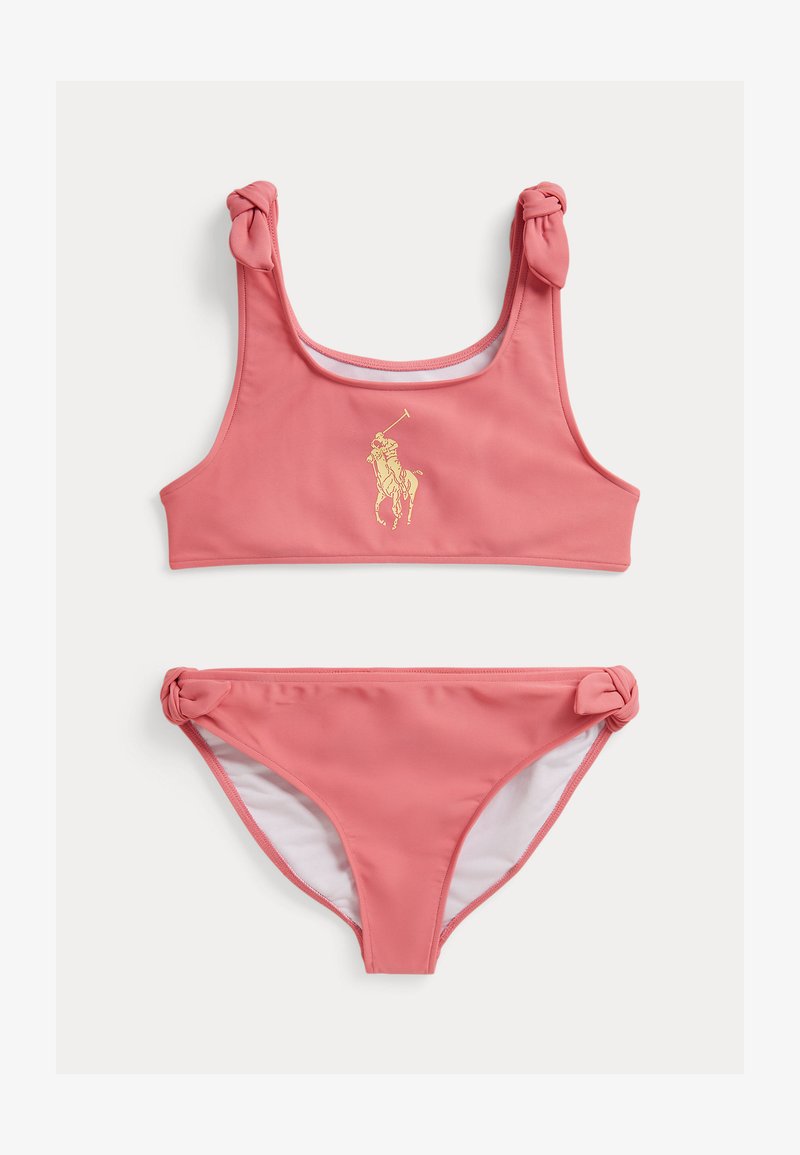 Σετ ροζ μπικίνι με τοπ τύπου tank με δεμένους ιμάντες και χρυσό λογότυπο, και αντίστοιχα κάτω μέρη με δεμένους κόμπους στα πλάγια.
