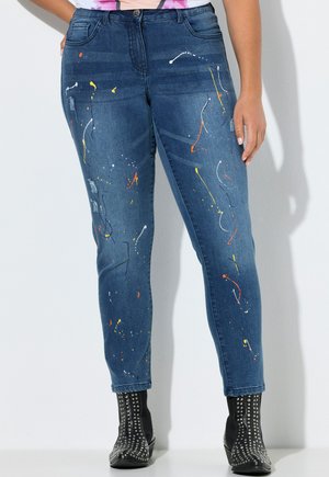 Denim jeans med farverige malingsprøjt detaljer, båret med sorte ankelstøvler med nitter.