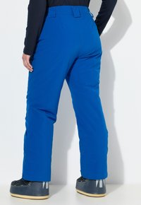 Modré zateplené lyžařské kalhoty s přímým střihem nohavic, vybavené poutky na opasek a hladkou, voděodolnou tkaninou. Doplněné černými lyžařskými botami.