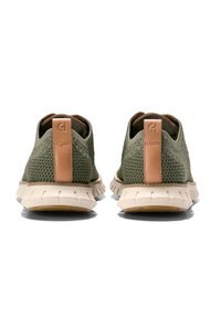 Zelené síťové tenisky s béžovou gumovou podrážkou, vybavené hnědým koženým poutkem na patě a texturovaným designem pro prodyšnost a podporu.