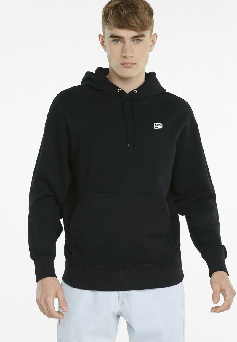 Schwarzer Hoodie aus einem Baumwollmischmaterial, mit einer vorderen Kängurutasche, gerippten Bündchen und einem kleinen Logopatch auf der Brust.