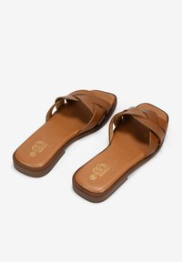 Sandalias de piel marrón con tira trenzada y punta cuadrada. La suela es plana con una textura suave y un logo grabado en la plantilla.