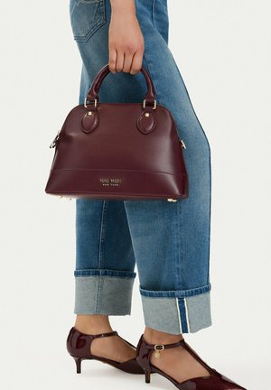 Kvinde iført opsmøgede blå jeans og burgunderrøde lave hæle, der holder en matchende burgunderrød Nine West taske.