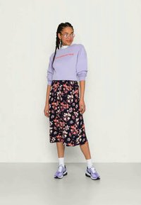 Sweatshirt lilás com texto vermelho, emparelhado com uma saia midi de flores escuras com flores rosa e brancas, complementado por ténis roxos e meias brancas.