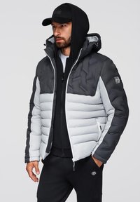 Vadderad jacka i svart och ljusgrå, med dragkedjestängning, huva och en blandning av släta och texturerade tyger. Slim fit-design med fickor.