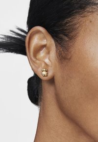 Pendientes de oro en exhibición, con un diseño de burbuja doble redondeada y una textura suave. Llevados en la oreja de una persona.