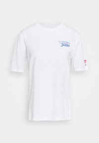 T-shirt en coton blanc à manches courtes, avec le texte bleu "Tommy Jeans" sur la poitrine et un logo de cœur rouge sur la manche gauche.